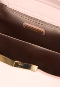 Innenansicht einer rosa Lederhandtasche mit glatter Textur, ausgestattet mit einem goldfarbenen Verschluss und einem braun ausgekleideten Fach.