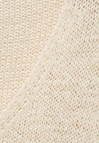 Kremno obarvana pletenina z dvema različnima teksturama: ena je gosta tkanina, medtem ko ima druga ohlapen, odprt vzorec.