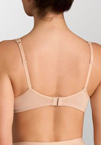 Reggiseno beige, leggermente imbottito, con spalline regolabili, chiusura a gancio e design senza cuciture sulla schiena, realizzato in un tessuto morbido ed elastico.