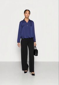 Blusa azul marinho de cetim com mangas longas, gola e três botões, combinada com calças pretas de cintura alta e saltos pretos de bico.