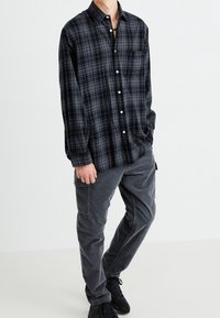 Zwart en grijs geruite flanellen blouse met een button-down kraag, lange mouwen en een borstvak, gecombineerd met grijze cargobroek en zwarte sneakers.