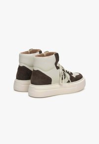 Bílé a hnědé semišové vysoké tenisky s texturovaným povrchem, kulatou špičkou a robustní bílou gumovou podrážkou s logovými akcenty.