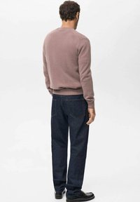 Sweter typu pulower w jasnym odcieniu mauve z okrągłym dekoltem, ściągaczami na mankietach i u dołu, zestawiony z ciemnoniebieskimi dżinsami z kieszeniami z tyłu.