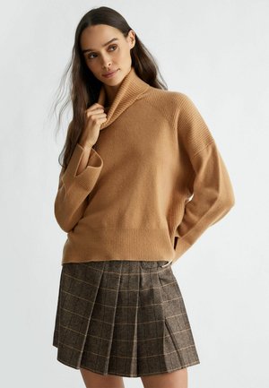 Maglione lavorato a maglia color sabbia con colletto alto e dettagli a coste, abbinato a una gonna a pieghe a quadri marrone con righe gialle.