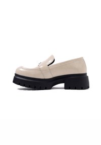 Mocassino in vernice beige con suola in gomma nera spessa. Presenta una punta tonda e una striscia decorativa sulla parte superiore.