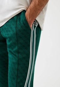 Pantaloni jogger verdi con motivo, caratterizzati da una trama sottile, strisce bianche sui lati e una vestibilità comoda. Mani inserite nelle tasche.