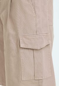 Shorts cargo en tissu beige avec une grande poche latérale à rabat sur la cuisse.