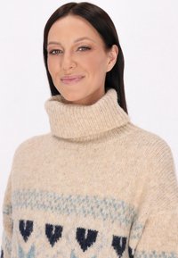 Pulover crem cu guler înalt, realizat dintr-un material tricotat texturat, având modele de inimi albastre și bleu, cu o croială lejeră și guler cu nervuri.