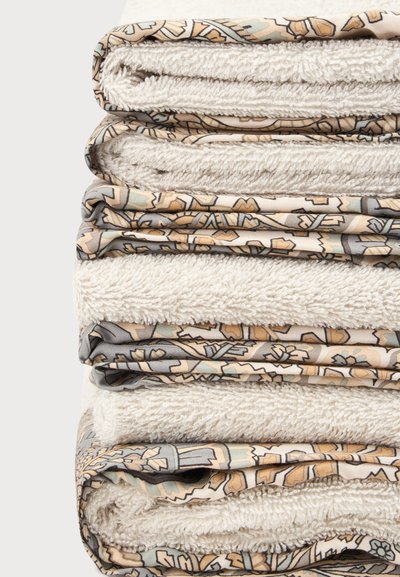 Pile de serviettes beiges pliées avec des bords en tissu à motifs dans des tons terreux atténués sur un fond uni.