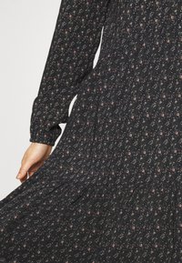 Černé šaty s dlouhým rukávem a květinovým vzorem v červené a bílé barvě. Lehce splývavý materiál s nařasením v pase a plisé sukní.