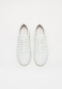 Baskets blanches en cuir avec bout rond, surface texturée et design à lacets. Comprend une semelle en caoutchouc contrastante avec de petites nodules.