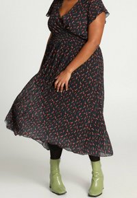 Robe midi noire à motifs floraux rouges et verts, avec manches courtes volantées et taille froncée, associée à des bottines vertes.