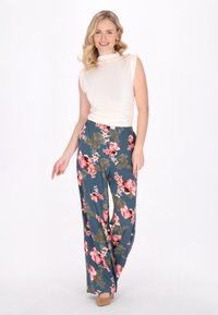 Lichtbeige aansluitende top met korte mouwen; luchtige teal broek met grote roze en groene bloemmotieven; tan hakken; soepele stof textuur.