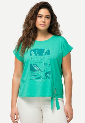 Camiseta verde de manga corta con escote redondeado, que presenta un estampado gráfico y un detalle de nudo en el dobladillo. Tela suave y ligera.