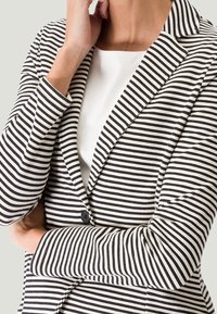 Blazer rayé en tissu noir et blanc, doté d'un col cranté, d'une fermeture à un bouton et d'une coupe ajustée avec une texture lisse.