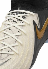 Scarpe sportive con tomaia in maglia bianca e nera, lacci e collare a calza nero. Accentuate da un logo Nike dorato e un lato nero texturizzato.