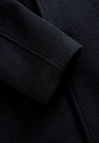 Manga de abrigo de lana negra con una textura suave y un detalle de costura ajustada, que muestra un color rico y profundo y una forma estructurada.