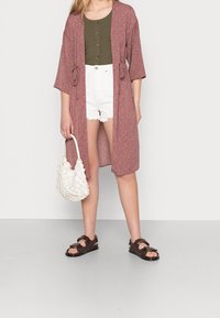 Maroon floral kimono with open front, tied at the waist, paired with a green tank, white shorts, and dark sandals. White textured handbag.