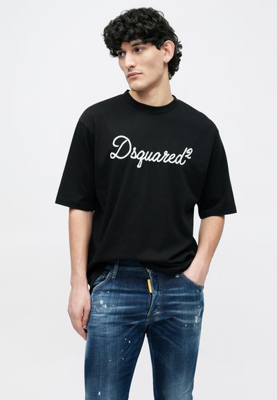 Black cotton t-shirt with "Dsquared²" logo in white script. Paired with faded blue jeans featuring speckled paint details.