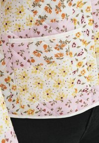 Tissu matelassé avec des motifs floraux en patchwork dans des tons de jaune, orange, marron et rose, présentant une poche rectangulaire bordée de blanc.