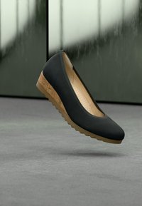 Μαύρο δερμάτινο παπούτσι με στρογγυλεμένη μύτη και χαμηλή σφήνα από φελλό στη σόλα. Στο εσωτερικό διαθέτει διάτρητη επένδυση για άνεση.