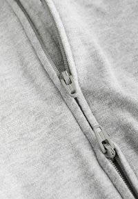 Grå zippered plagg med en mjuk, texturerad yta. Har en ljusgrå dragkedja och släta sömmar längs sömmen.