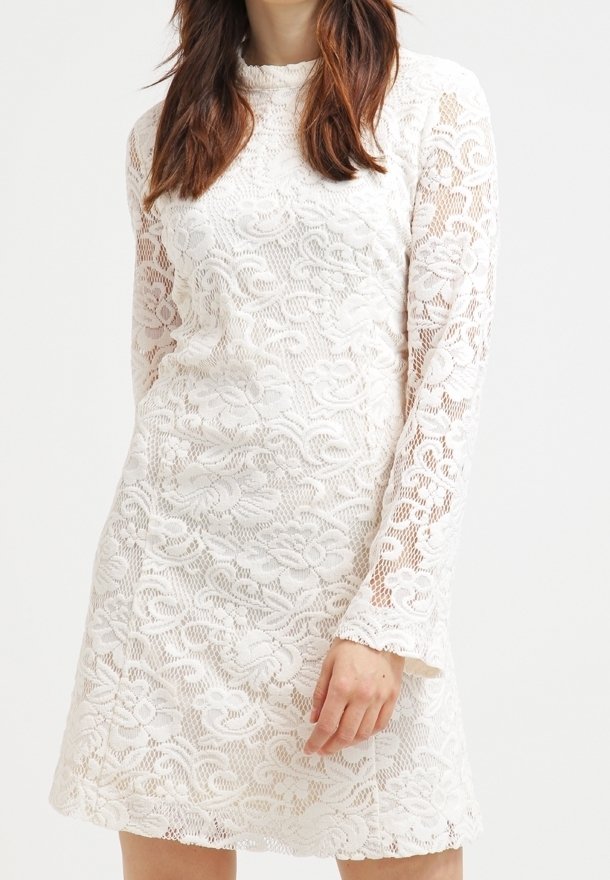 Robe blanche en dentelle avec manches longues, motif floral, tissu texturé et encolure ronde, présentant une légère silhouette évasée.