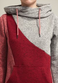 Hoodie color-blocked grigio e rosso con colletto a cowl, cordini e tasca frontale. Tessuto testurizzato con una finitura morbida.