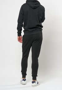 Svart hoodie med en avslappnad passform, ihop med matchande joggers. Slätt tyg, ribbade ärmslut och sidofickor ger funktionella detaljer.