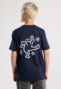 Navy blue cotton t-shirt featuring a large white graphic of a figure with lines on the back. Short sleeves, relaxed fit, standard neckline.