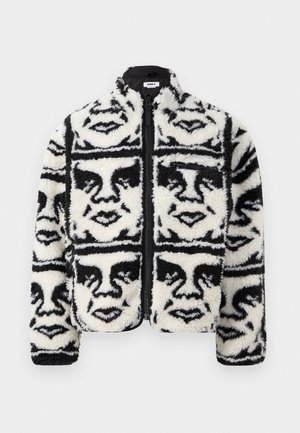 Fuzzy black and white zip-up jacket featuring a repeated graphic pattern of faces. Made of soft, textured fleece material.
