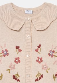 Beige cardigan med rund krage, med blomsterbroderi i rosa og blått, knapperekke foran, samt ribbestrikket krage og knapplist.