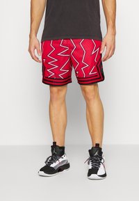 Röda sportshorts med ett zigzag-mönster och svarta detaljer, med en mesh-textur. Även kombinerade med svarta och vita högsnörda sneakers.