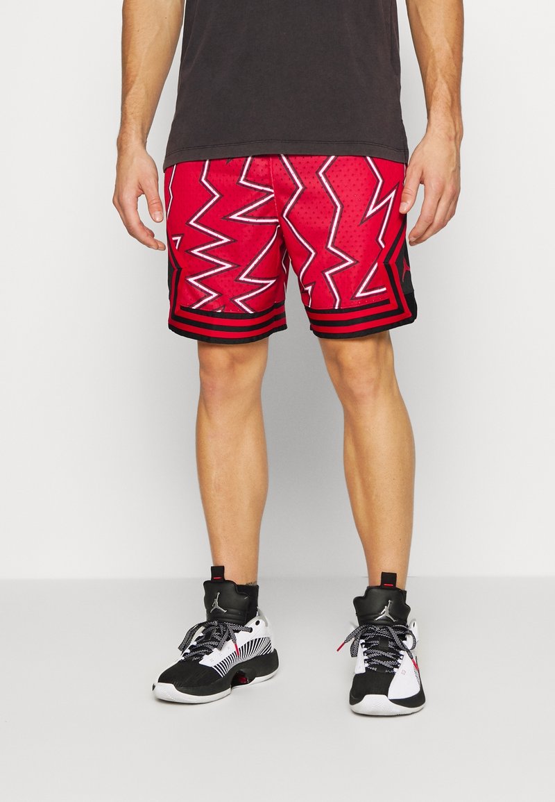 Röda sportshorts med ett zigzag-mönster och svarta detaljer, med en mesh-textur. Även kombinerade med svarta och vita högsnörda sneakers.