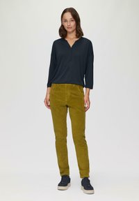 Dunkelblaues Langarmshirt mit V-Ausschnitt, kombiniert mit olivgrünen Cordhosen. Modell trägt dunkle Sneakers und steht vor einem neutralen Hintergrund.