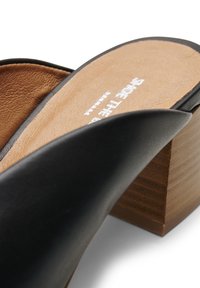 Svart lädersandal med gliddesign och en brun texturerad fotbädd samt en träblockklack. Har en bred remdesign och en slät yta.