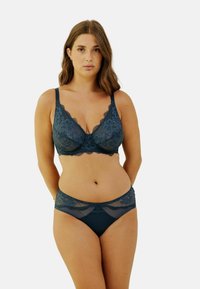 Soutien-gorge en dentelle teal foncé et bikini assorti, avec des motifs floraux et des accents en mesh, doté de bretelles réglables et d'un nœud décoratif central.