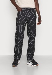 Pantalones de mezclilla negros con un patrón lineal blanco, que cuentan con un corte clásico, cinco bolsillos y un cierre de botón. Llevados con zapatillas negras.
