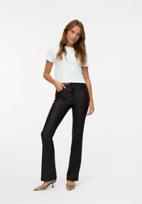 T-shirt blanc court associé à un pantalon évasé noir brillant et des chaussures à talons à motif serpent, le tout sur un fond blanc uni.