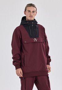 Maronfarvet pullover hoodie med sorte detaljer, en frontlomme, justerbar hætte og snore. Har branding i midten. Glat tekstur.