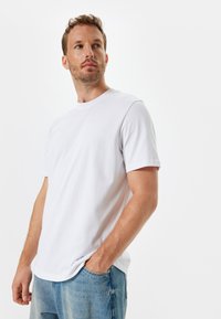 Witte crew-neck t-shirt van zachte katoen, met korte mouwen, een relaxte pasvorm en een gladde textuur. Gecombineerd met lichtblauwe denim jeans.