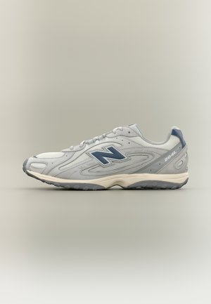 Αθλητικό παπούτσι New Balance 204L σε γκρι και λευκό με μπλε λογότυπο, επάνω μέρος από δίχτυ και σουέντ, και λαστιχένια σόλα, εμφανιζόμενο από το πλάι σε ουδέτερο φόντο.
