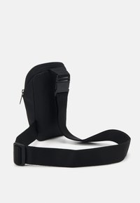 Bolso cruzado de tela negra con un diseño delgado, cierre con cremallera y correa ajustable. Superficie texturizada, estilo minimalista sin acentos adicionales.