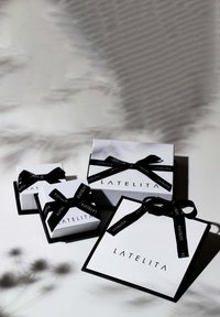 Three white gift boxes with black ribbons, featuring the "LATELITA" logo in black. Various sizes displayed against a light background.