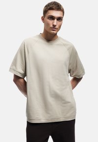 Beige kortærmet t-shirt lavet af bomuld, med en afslappet pasform, rund halsåbning og raglanærmer, med en glat tekstur.
