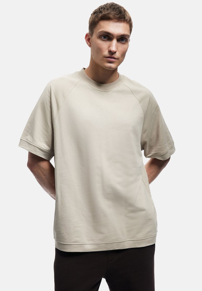 Beige kortærmet t-shirt lavet af bomuld, med en afslappet pasform, rund halsåbning og raglanærmer, med en glat tekstur.