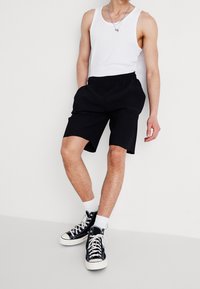 Pantalones cortos negros de canalé con cinturilla elástica, combinados con una camiseta sin mangas blanca y zapatillas altas negras con cordones blancos y calcetines.