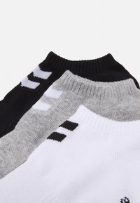 Tre paia di calzini alla caviglia in nero, grigio e bianco. Tessuto lavorato a maglia con polsini a coste e strisce del logo del marchio in contrasto sui lati.