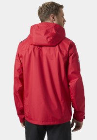 Czerwona wodoodporna kurtka z kapturem, o gładkiej fakturze i regulowanymi mankietami. Logo na lewym rękawie. Widok z tyłu.