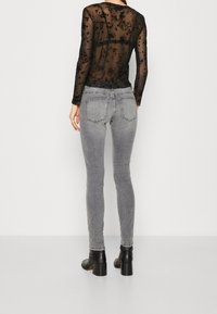 Svart genomskinlig långärmad topp med blommönster, som matchas med åtsittande grå denimjeans och svarta klackstövlar.